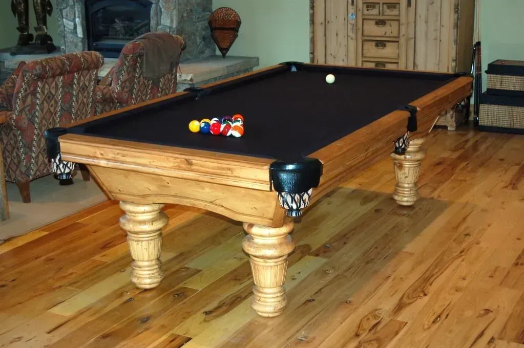 Pool table in a room with hardwood floors. Balls are racked at one end, one ball in play.
