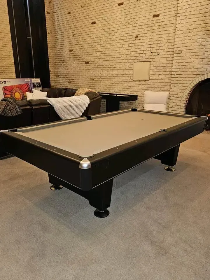 Black pool table with gray felt in a room with a brick wall and couches.