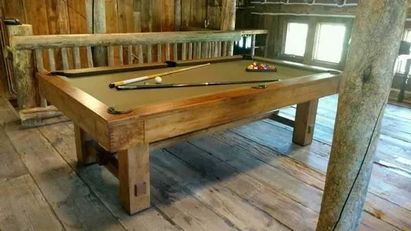 Pool table in rustic wooden room, with cue sticks and balls on the green felt surface.