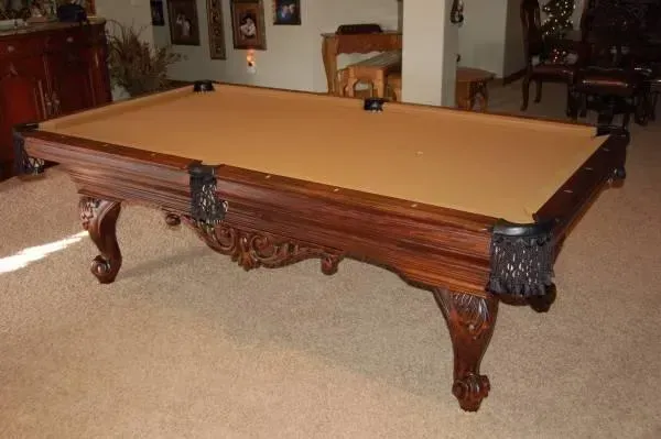 Ornate brown pool table with tan felt, indoors.