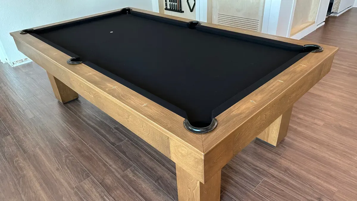 A light wood pool table with black felt on a wood floor.