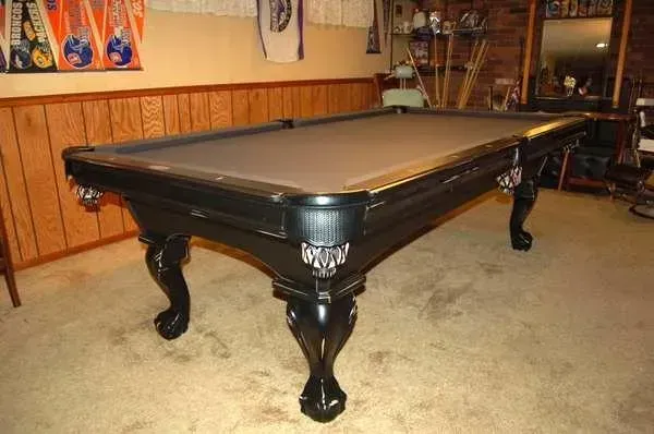 Black pool table on carpet, in a room with wood paneling and sports memorabilia.