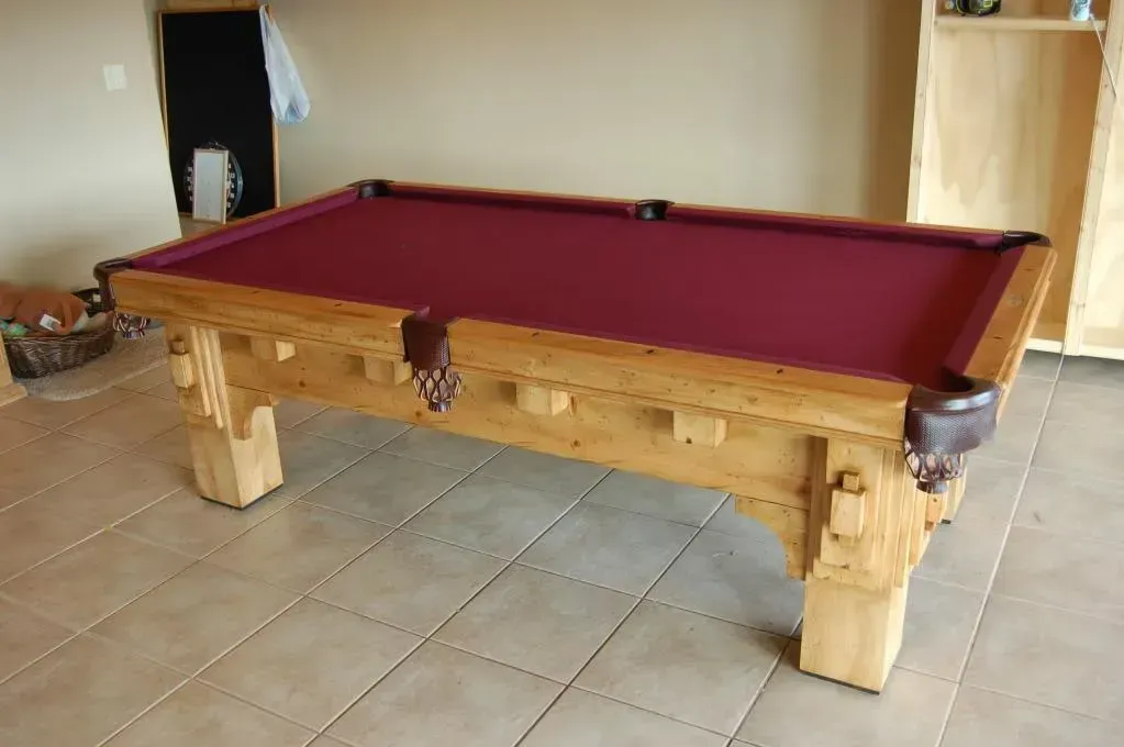 Pool table with burgundy felt and light wood frame, set on tiled floor.
