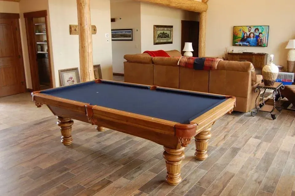 Pool table with blue felt in a home with wooden floors and a couch.