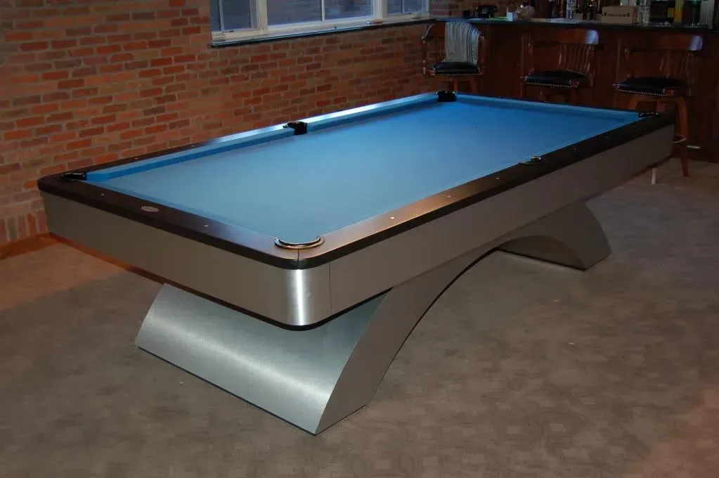 Modern silver pool table with blue felt in a brick-walled room.