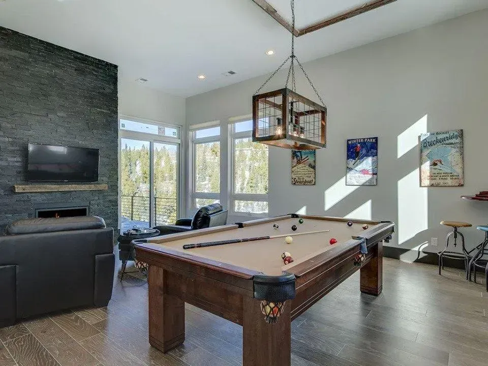 Pool table in a game room with dark wood floors, large windows, and a hanging light fixture.