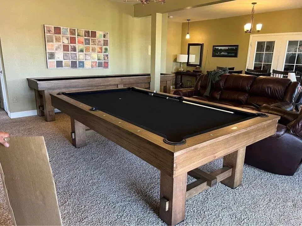A pool table and shuffleboard in a game room with a brown leather sofa and art.