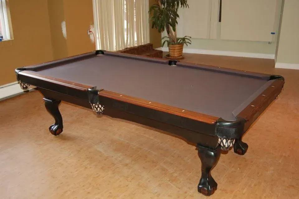 Dark brown pool table on a light brown floor. The table has dark legs and a brown cloth.