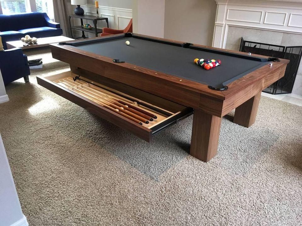 Pool table with drawer holding cues, balls set, in a living room. Dark wood and black felt.