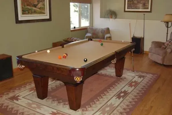 Pool table in a room with a rug, balls, and surrounding furniture.