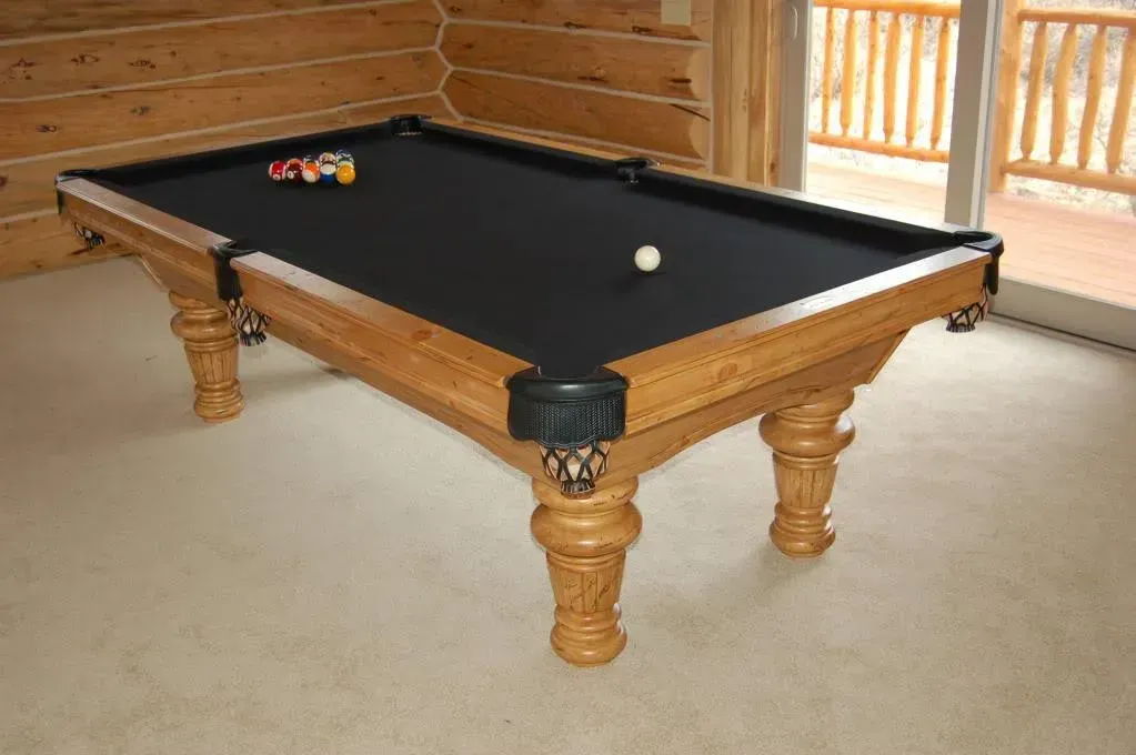 Wooden pool table with black felt, balls set up, and a white cue ball.