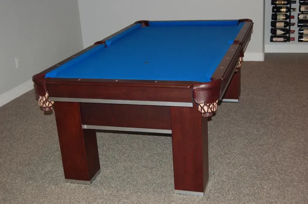 Pool table with blue felt and brown wood in a carpeted room.
