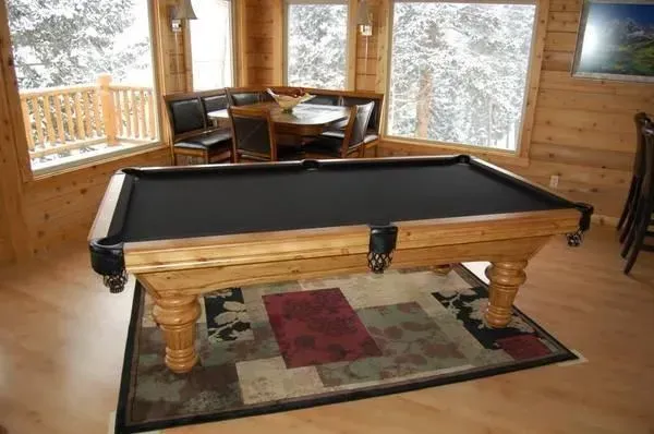 Wooden pool table with black felt in a wood-paneled room, with a snowy outdoor view.