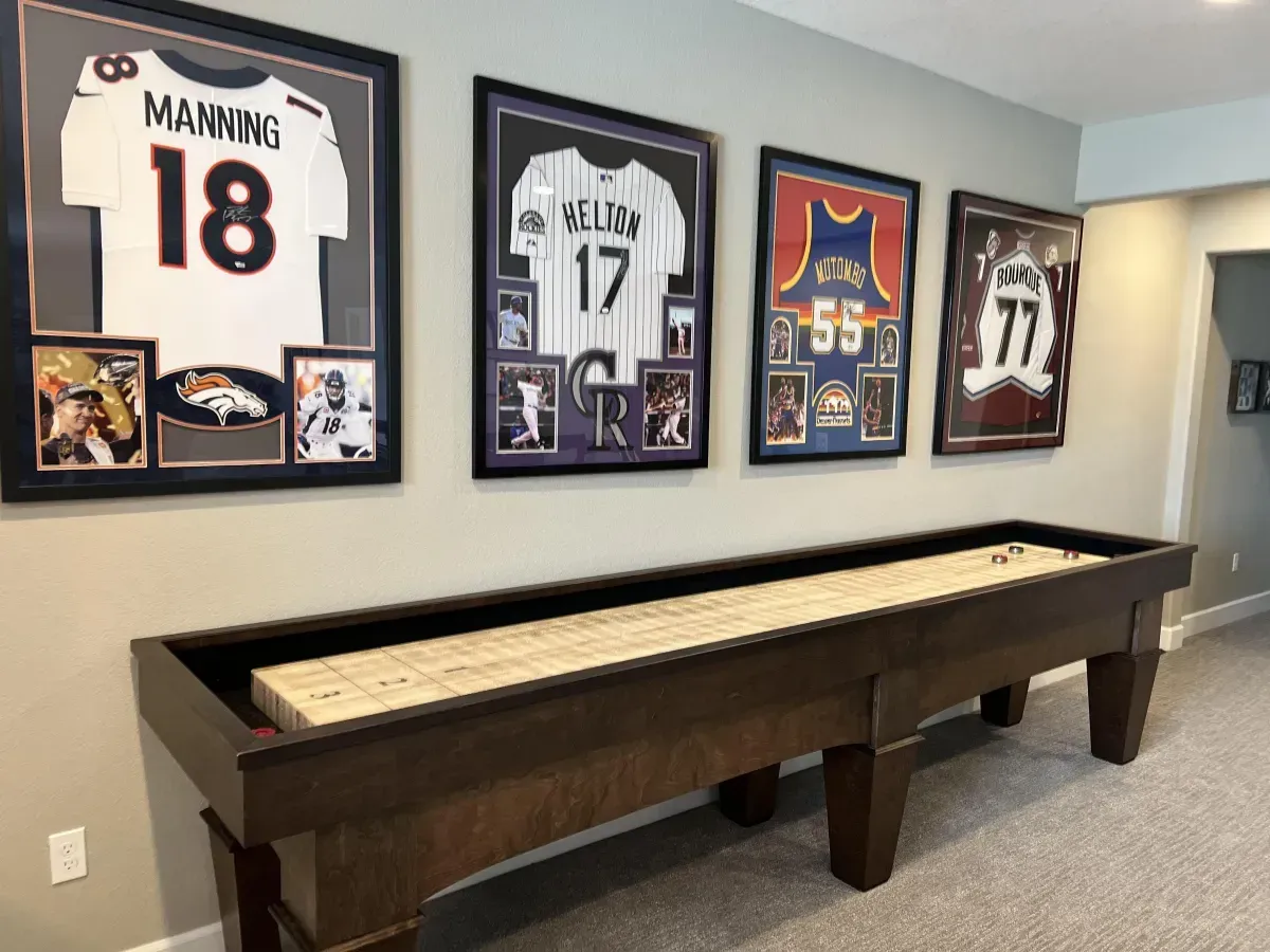 Shuffleboard table in a game room with framed sports jerseys on the wall.