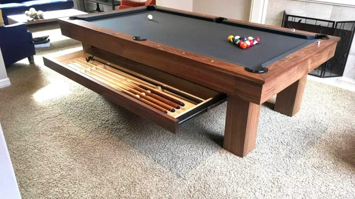Pool table with a drawer holding pool cues, set in a carpeted room.