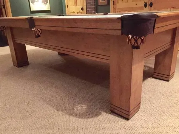 Wooden pool table with brown felt and ball pockets in a carpeted room.