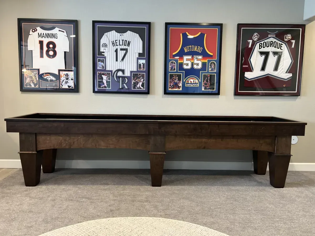 Pool table with framed sports jerseys on the wall above it.