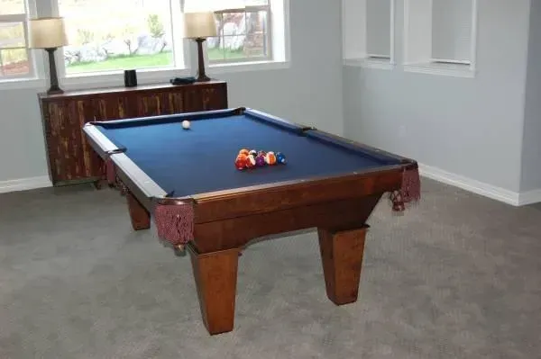 Pool table in a room with a blue felt top, surrounded by balls and a cue ball.