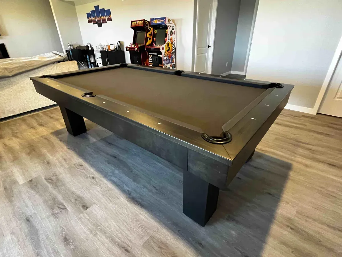 Pool table with black felt in a game room with arcade games.