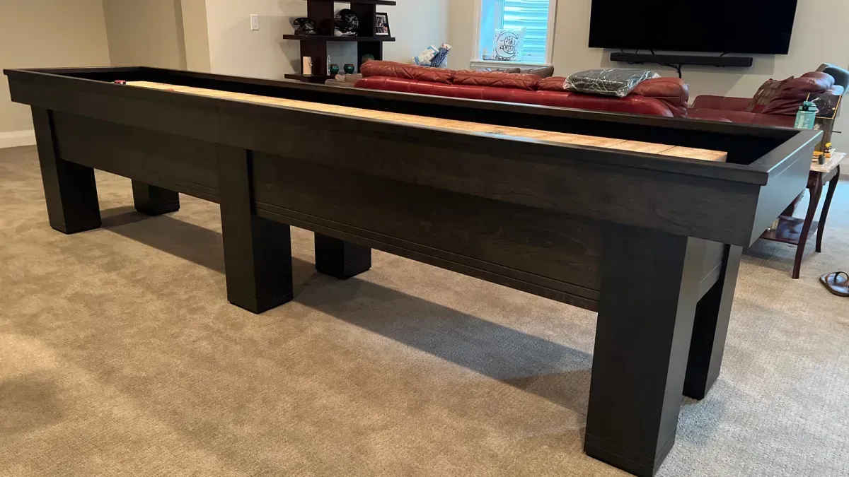 Dark wooden shuffleboard table on a carpeted floor.