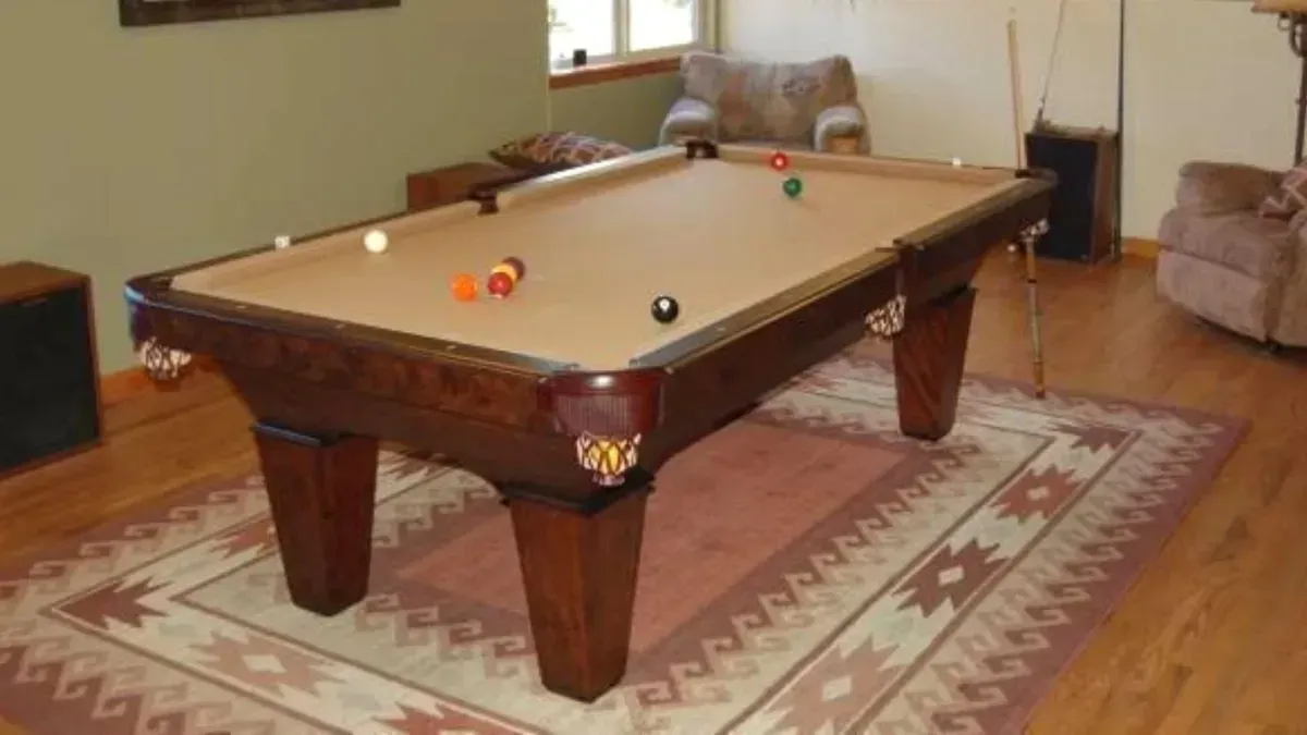 Pool table with balls on a patterned rug, set in a room with wood flooring.