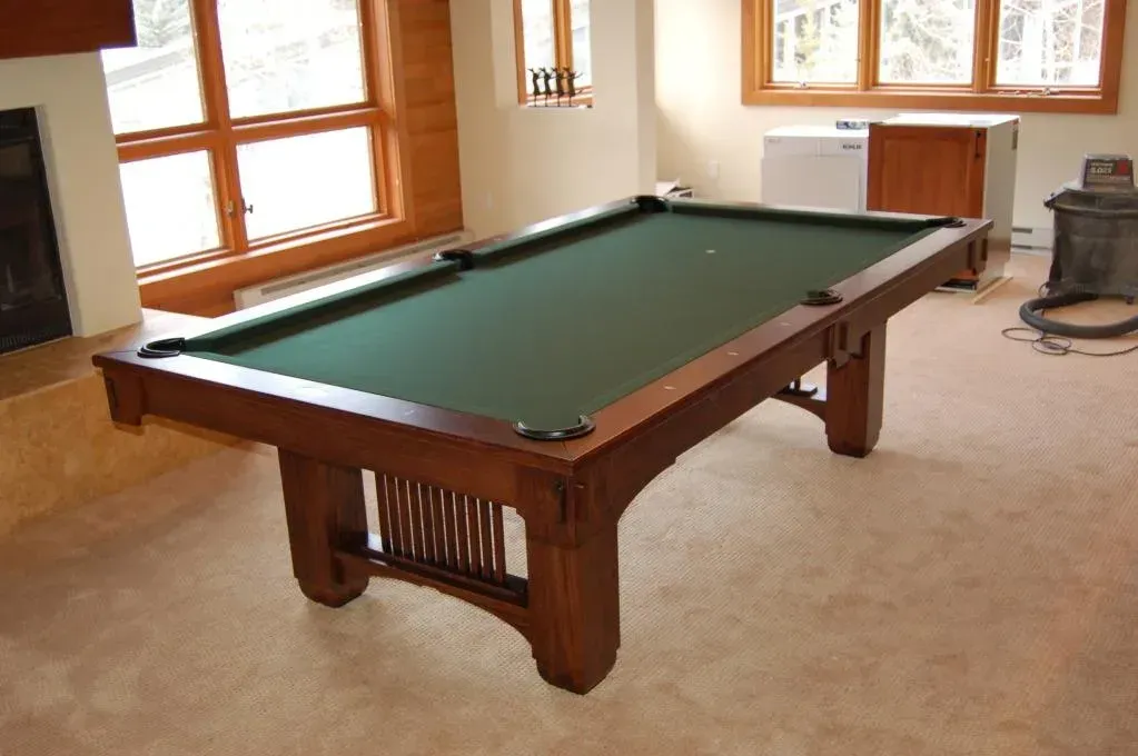 A wooden pool table with green felt in a room with windows and light-colored carpet.