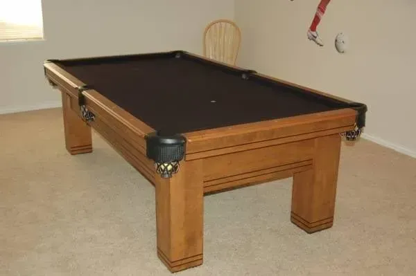 Wooden pool table with black felt in a carpeted room.