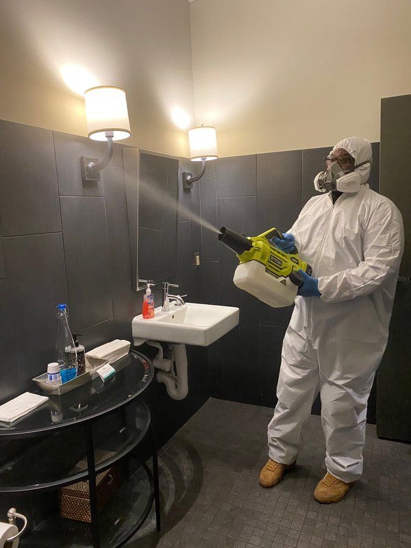 A man in a protective suit is spraying a bathroom with a sprayer.