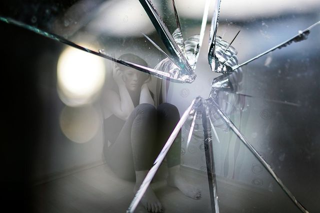 A woman is sitting in front of a broken mirror.