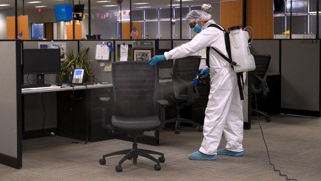 A man in a protective suit is disinfecting an office chair.