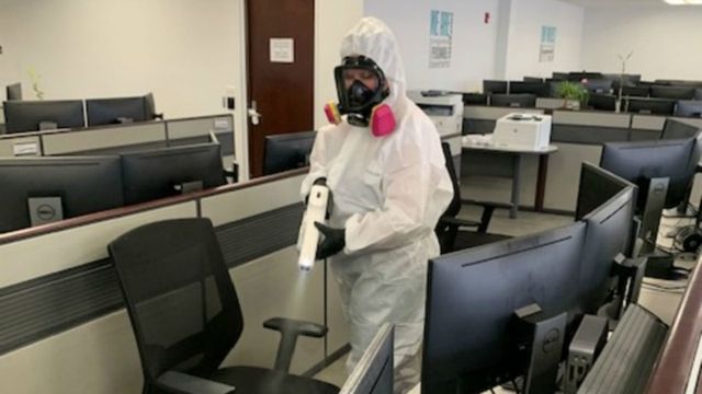 A man in a protective suit is disinfecting an office.