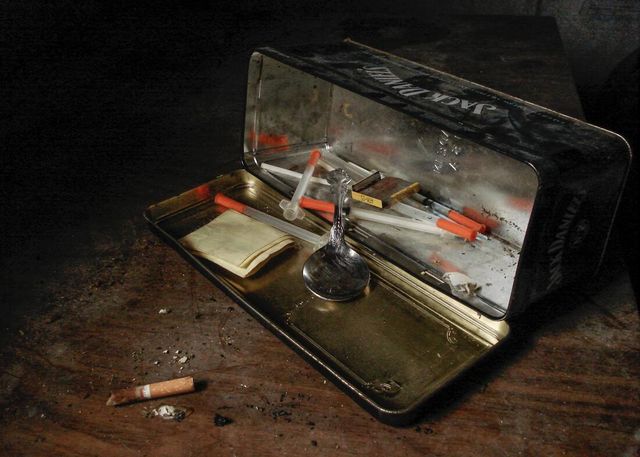 A tin filled with syringes and cigarettes on a table