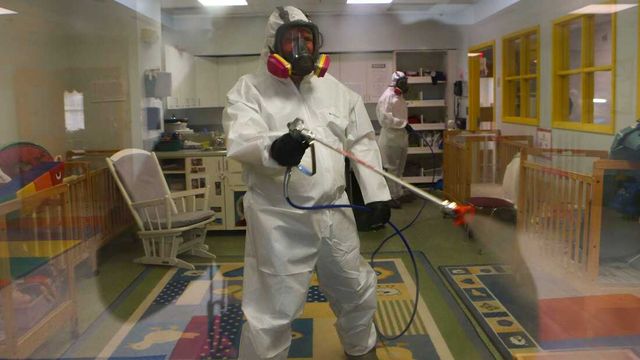 A man in a protective suit is spraying a room with a sprayer.