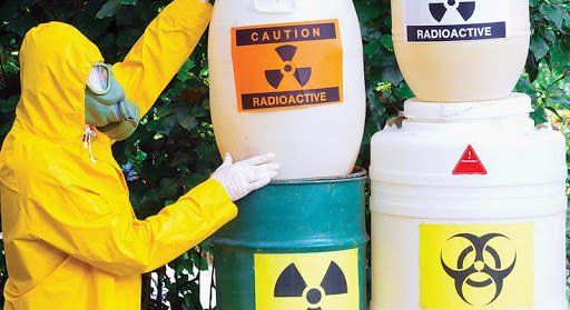 A person in a yellow suit is holding a barrel with a radioactive label on it.