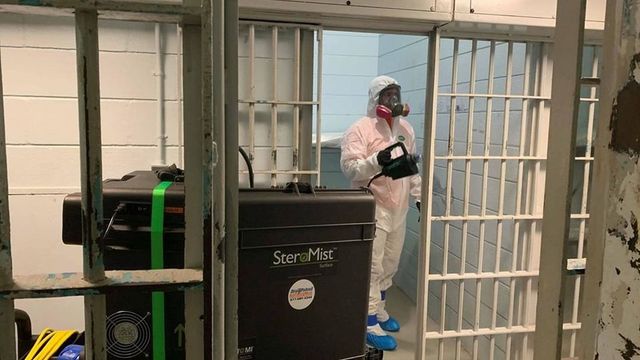 A man in a protective suit is disinfecting a prison cell.