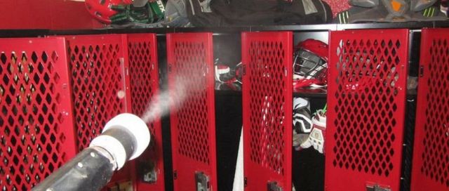 A person is spraying water on a row of red lockers in a locker room.