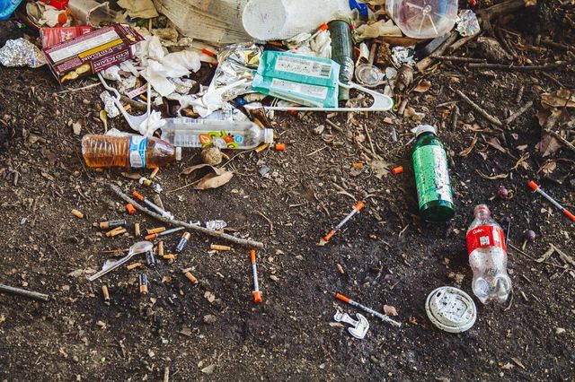 A pile of trash on the ground with syringes and bottles.