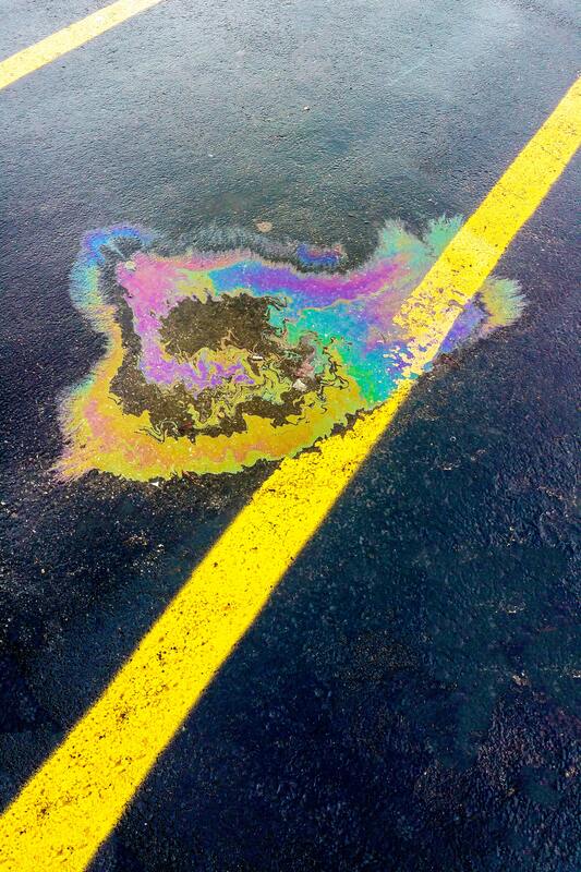 A puddle of oil on the ground next to a yellow line.