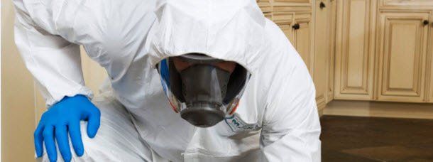 A man in a white suit and blue gloves is wearing a gas mask.