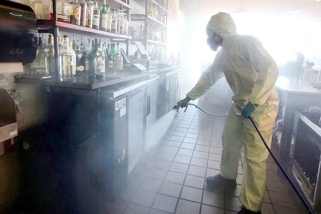 A man in a protective suit is spraying a kitchen with a sprayer.