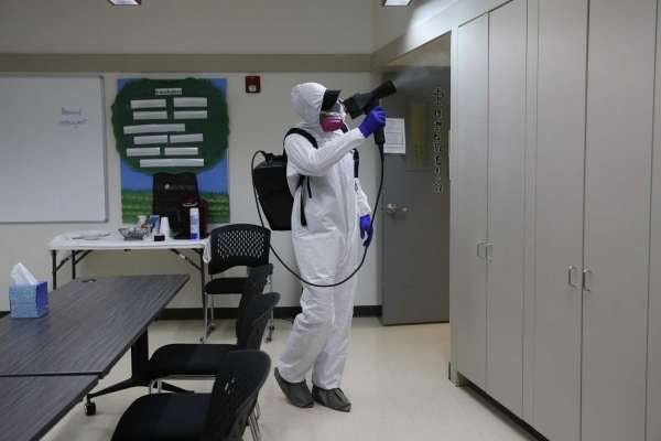 A man in a protective suit is spraying a room with a sprayer.