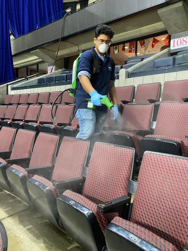 A man wearing a mask and gloves is spraying seats in an auditorium.