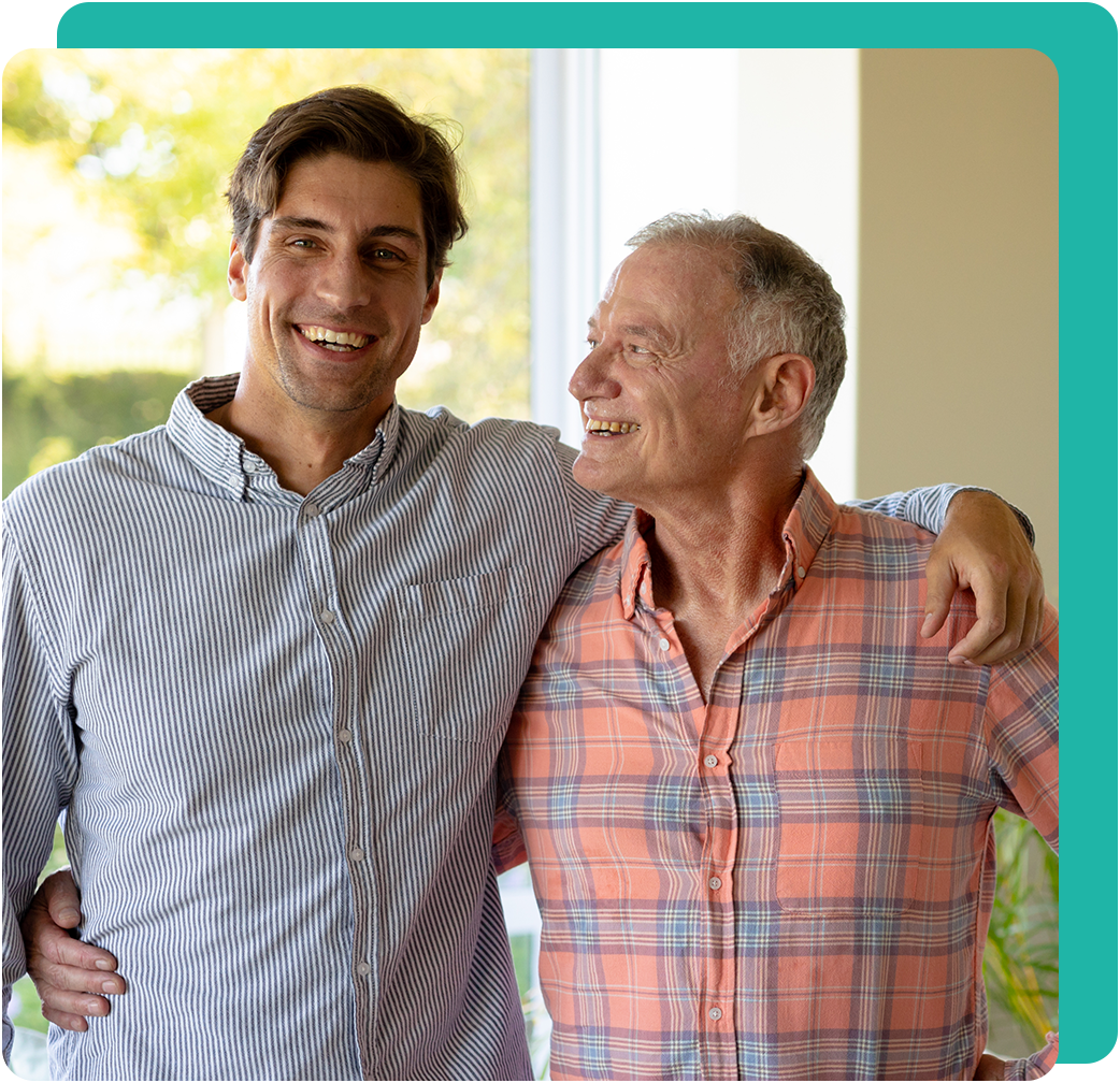Two men, smiling, embracing, outdoors. One in striped shirt, other in orange plaid.