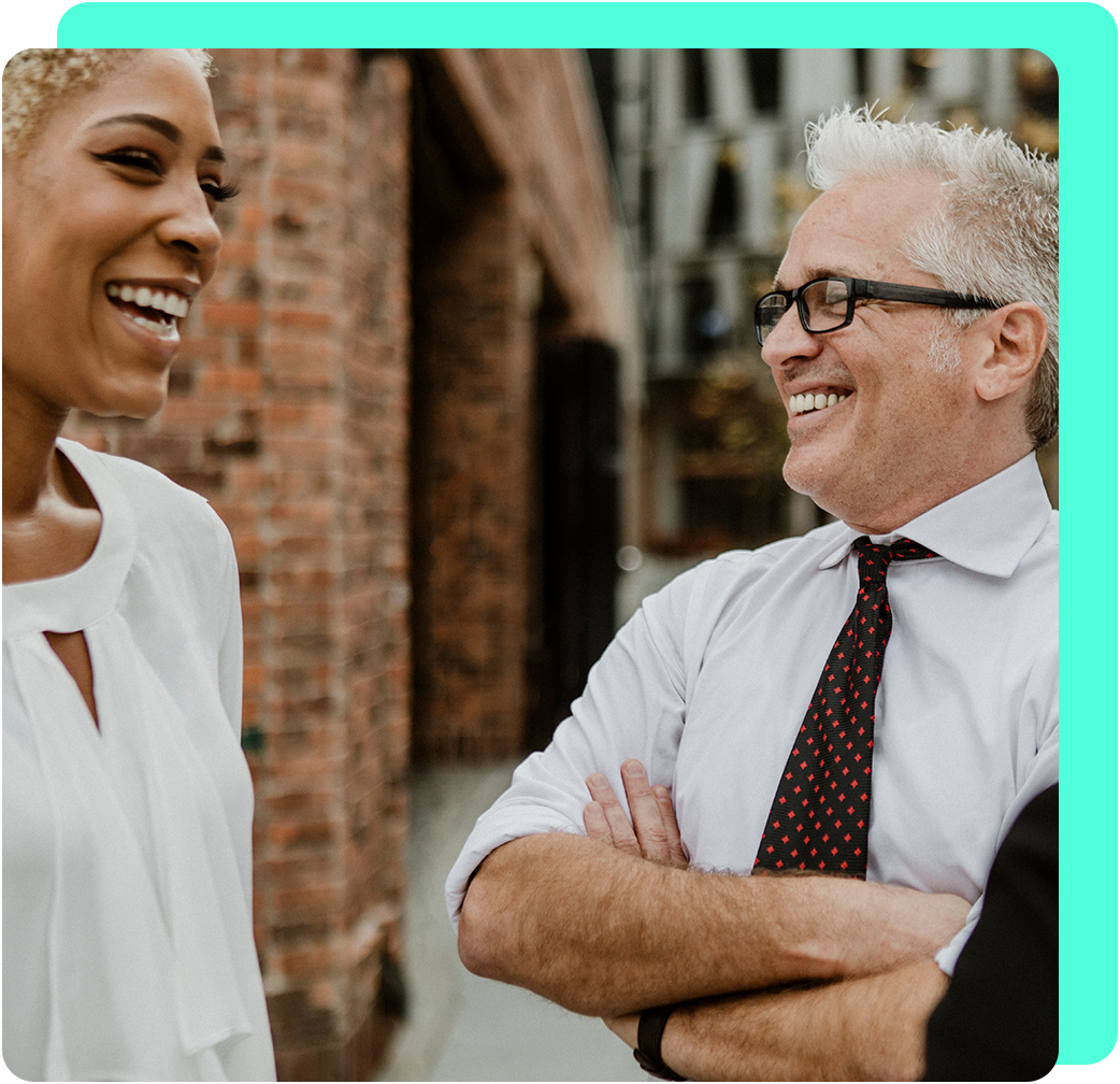 Woman and man smiling while talking outside near a brick building.