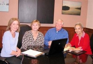 Four people, two women and two men, seated around a table, working with a laptop.