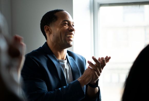 Man in blue blazer applauding, smiling in an office setting.