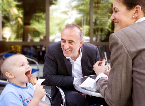 A family, smiling and enjoying ice cream outdoors. A child eats a cone, while the parents laugh.