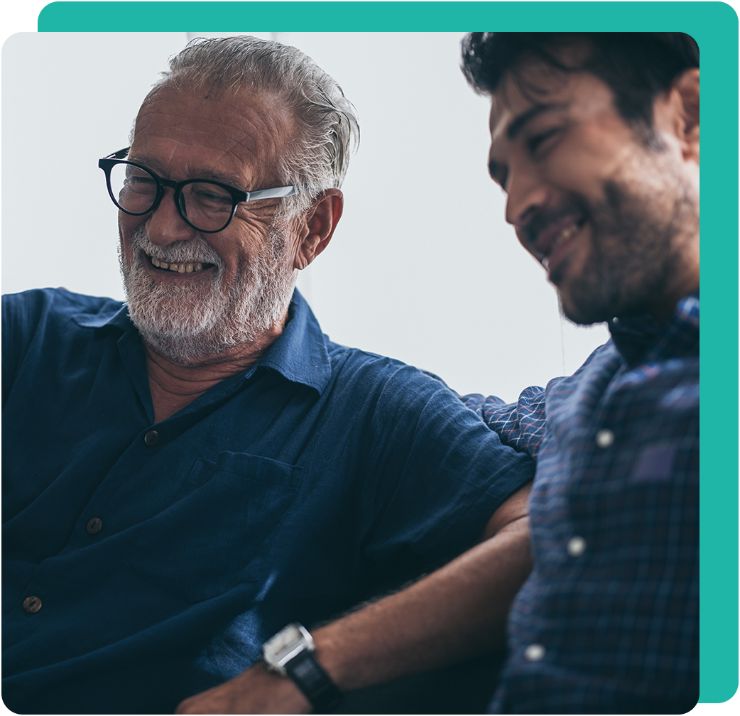 Older man with glasses and younger man smiling, indoors.