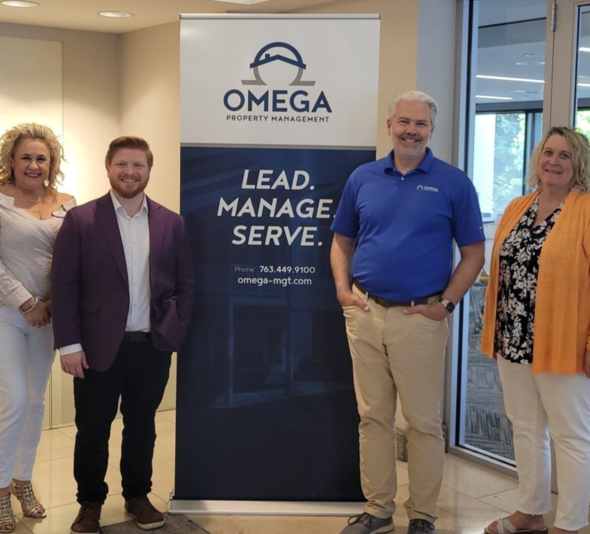 Four people pose in front of a banner for Omega Property Management.