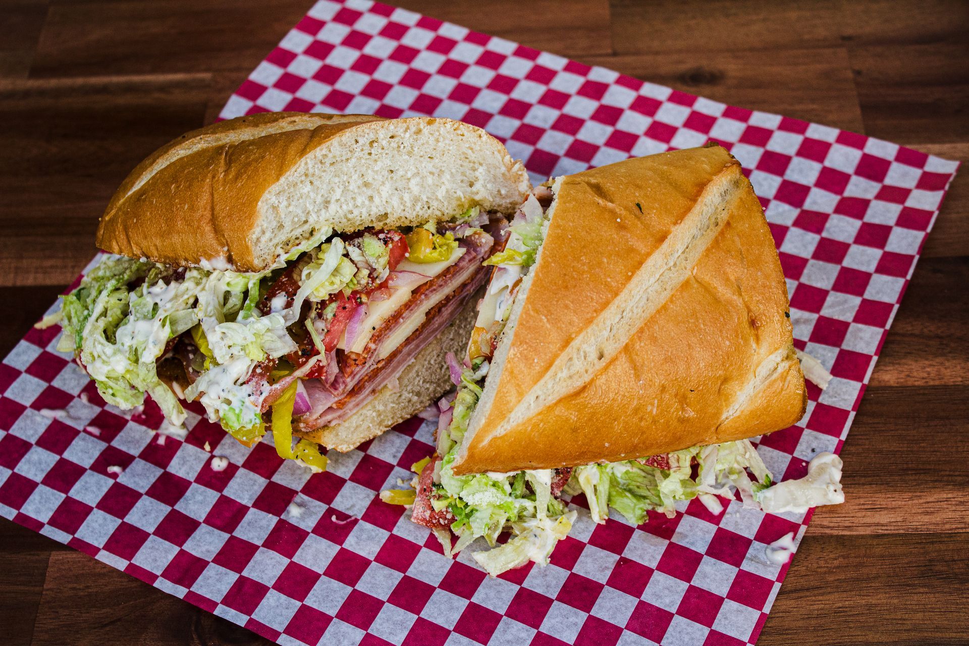 Sub sandwich cut in half, with meat, cheese, and slaw on red checkered paper.